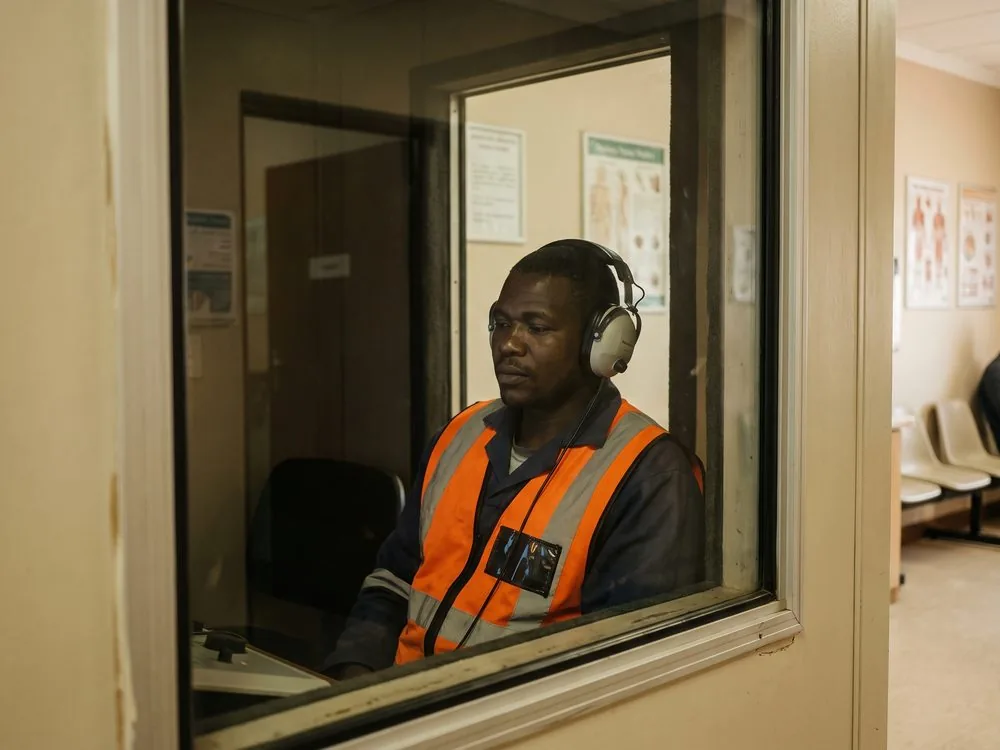 A worker undergoing an audiometric test inside a soundproof booth, seen through the observation window