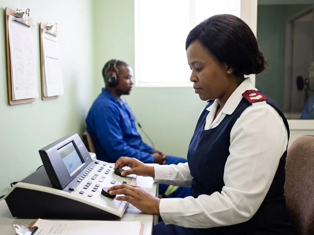 An occupational health nurse operating the audiometer console during a hearing test